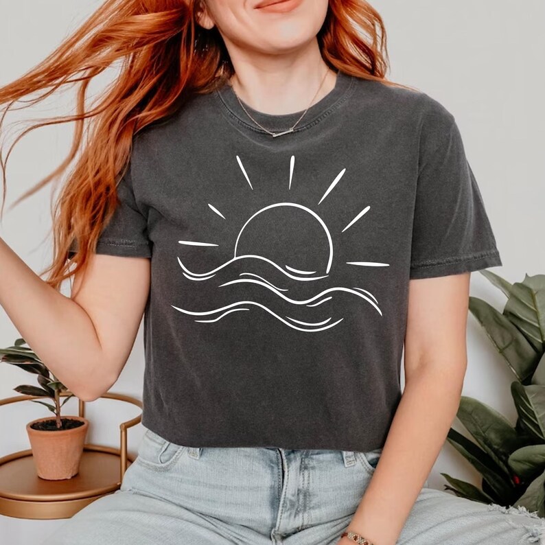 May include: A dark gray cropped t-shirt with a white graphic of a sun setting over waves.