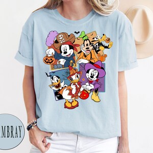 K&ouml;nnte beinhalten: Hellblaues T-Shirt mit einem Grafikdruck von Mickey Mouse, Minnie Mouse, Donald Duck, Goofy und Pluto in Halloween-Kost&uuml;men. Die Figuren halten K&uuml;rbisse und S&uuml;&szlig;igkeiten.