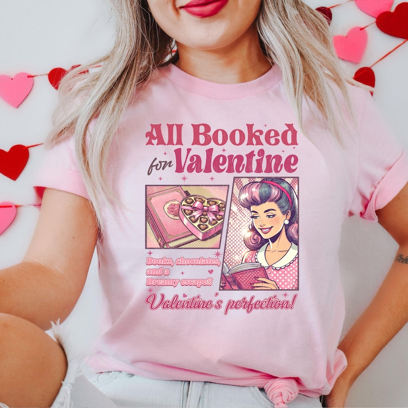 Puede incluir: Camiseta rosa con un dise&ntilde;o gr&aacute;fico que dice "All Booked for Valentine" con una imagen de dibujos animados de una mujer leyendo un libro y una caja de chocolates. El texto debajo de la imagen dice "Books, chocolates, and a dreamy escape! Valentine's perfection!"