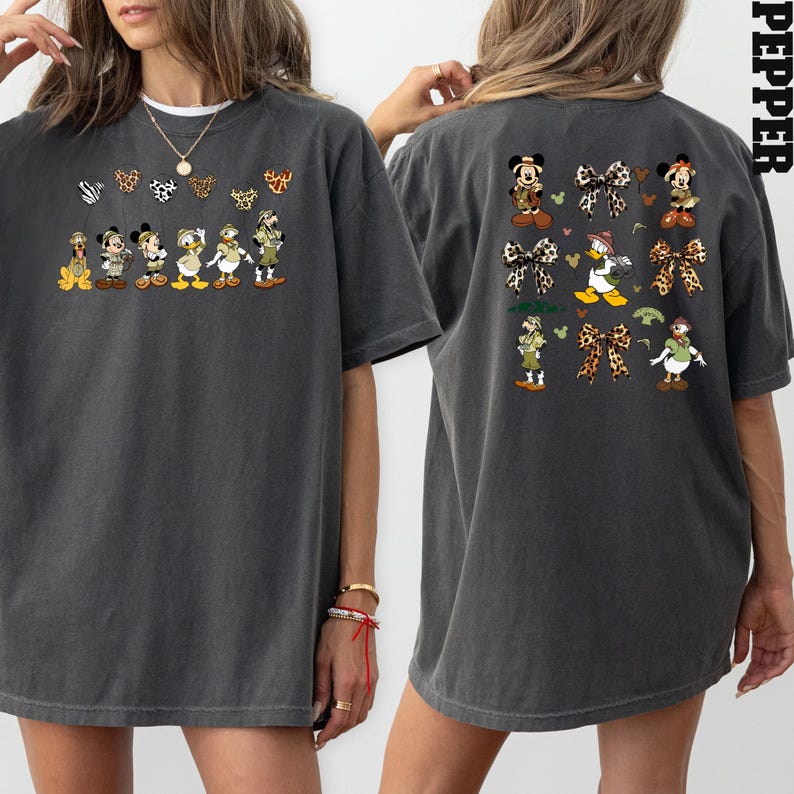 May include: A gray oversized t-shirt with a graphic print of Disney characters dressed in safari outfits. The front of the shirt features a line of characters, while the back features a grid of characters and bows. The shirt has a relaxed fit and short sleeves.