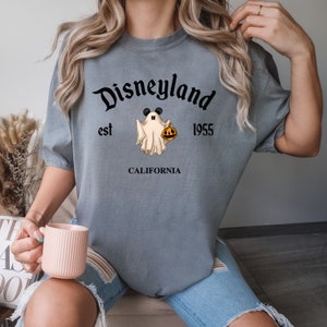 Puede incluir: Una camiseta gris con el texto "Disneyland est 1955 CALIFORNIA" y un fantasma de dibujos animados con orejas de Mickey Mouse y sosteniendo una calabaza.
