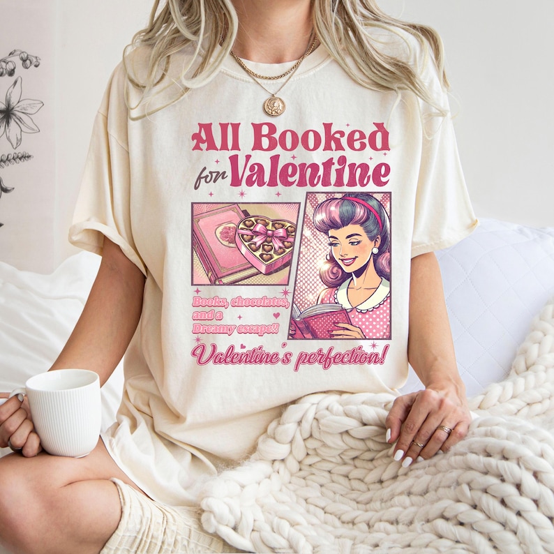 Puede incluir: Una camiseta blanca con el texto "All Booked for Valentine" en letras rosas y negras. El dise&ntilde;o presenta una mujer de dibujos animados leyendo un libro y una caja de chocolates. El texto debajo de la imagen dice "Books, chocolate, and a dreamy escape! Valentine's perfection!"