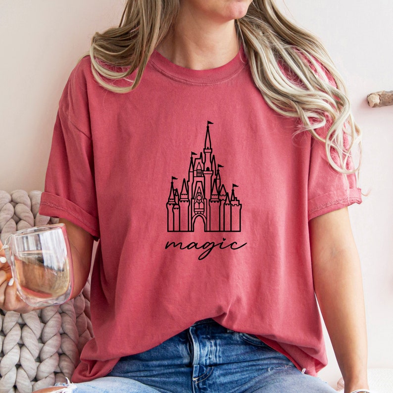 May include: A red t-shirt with a black outline of Cinderella's castle and the word "magic" written underneath.