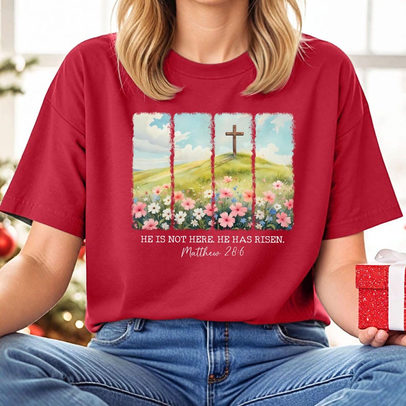 May include: Red t-shirt featuring a graphic of a cross on a hill with flowers and the text "He is not here. He has risen. Matthew 28:6"