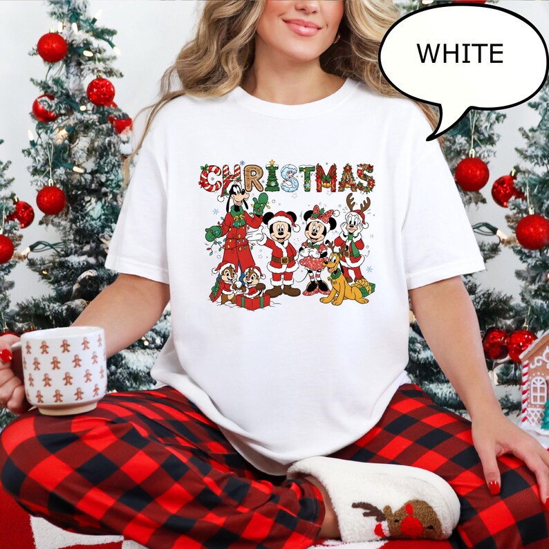 May include: White t-shirt with a colourful Christmas graphic featuring cartoon characters. The word "CHRISTMAS" is displayed across the top in a festive font. The characters include Mickey and Minnie Mouse, Goofy, and Pluto.