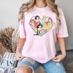 Pu&ograve; includere: Una maglietta rosa con un design a forma di cuore che presenta sette principesse Disney: Biancaneve, Cenerentola, Ariel, Jasmine, Belle, Aurora e Rapunzel.