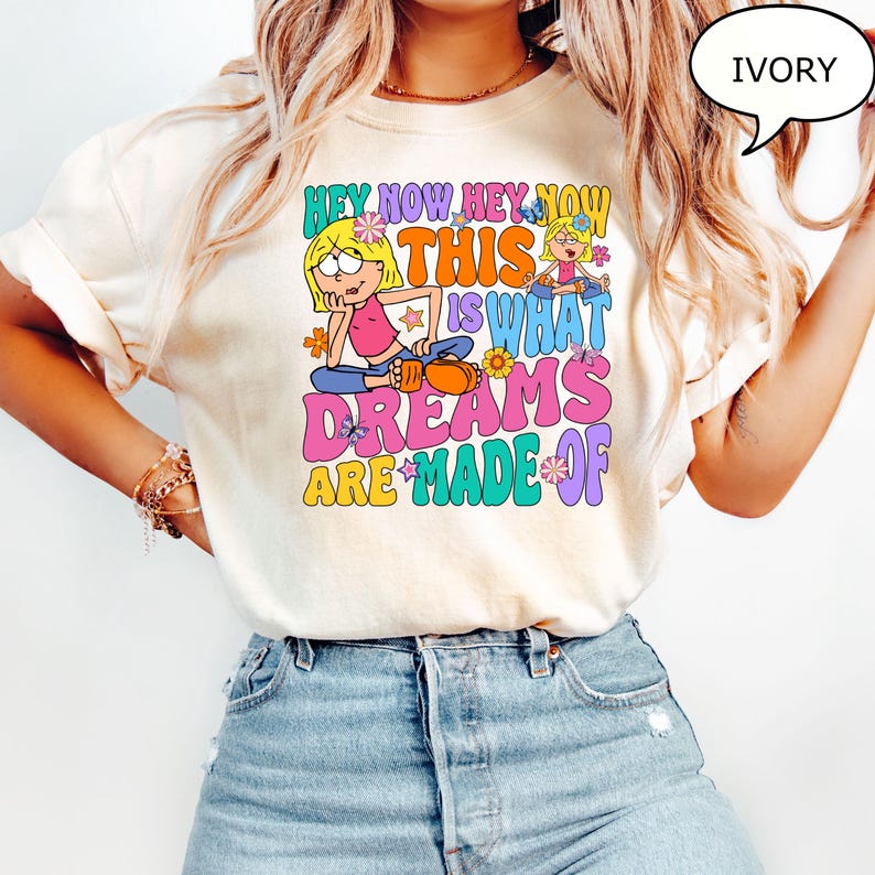 Może przedstawiać: Biały T-shirt z nadrukiem graficznym przedstawiającym dwie kresk&oacute;wkowe dziewczyny i tekst "Hey Now Hey Now This Is What Dreams Are Made Of". Tekst jest w kolorowej retro czcionce z kwiatami i motylami.