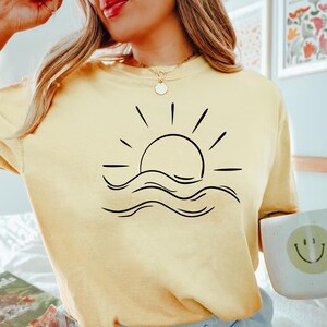 May include: A yellow t-shirt with a black graphic of a sun setting over waves.