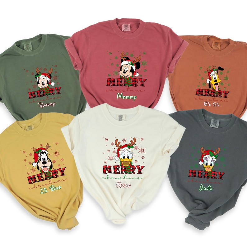 Op de afbeelding: Zes verschillende T-shirts met een kerstthema met Mickey Mouse, Donald Duck en Goofy. Elk shirt heeft een andere naam, waaronder "Daddy", "Mommy", "Big Sis", "Lil Bro", "Aldo" en "Julie".