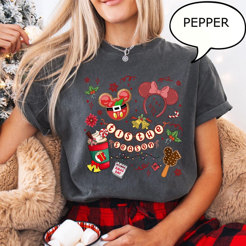 May include: Dark grey t-shirt with a festive holiday design. The shirt features a Mickey Mouse gingerbread cookie, a Minnie Mouse bow headband, and the phrase "'Tis the Season". Other graphics include a coffee cup, candy canes, and a Christmas Day calendar.