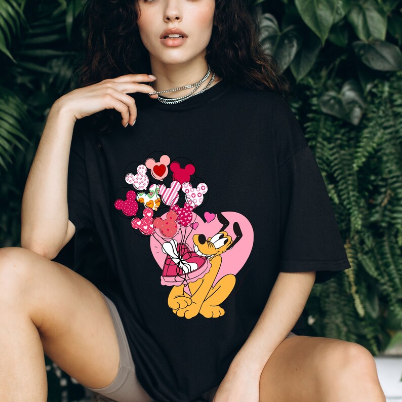 Może przedstawiać: Czarny t-shirt z kresk&oacute;wkową postacią Plutona trzymającego pudełko w kształcie serca i wiązkę balon&oacute;w z sercami i kropkami.