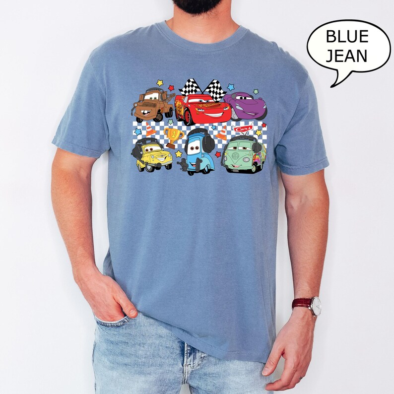 May include: A blue jean t-shirt with a graphic print of cartoon cars from the movie Cars. The cars are in a checkered pattern with stars and a trophy. The text "Cawa Zoom" is on the shirt.