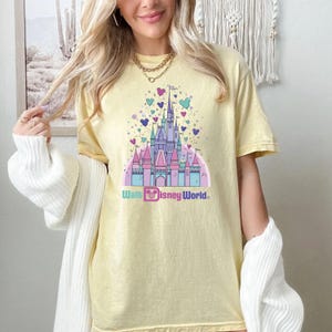 May include: A yellow t-shirt with a graphic of Cinderella's castle and the text "Walt Disney World." The castle is surrounded by pink, purple, and blue balloons.
