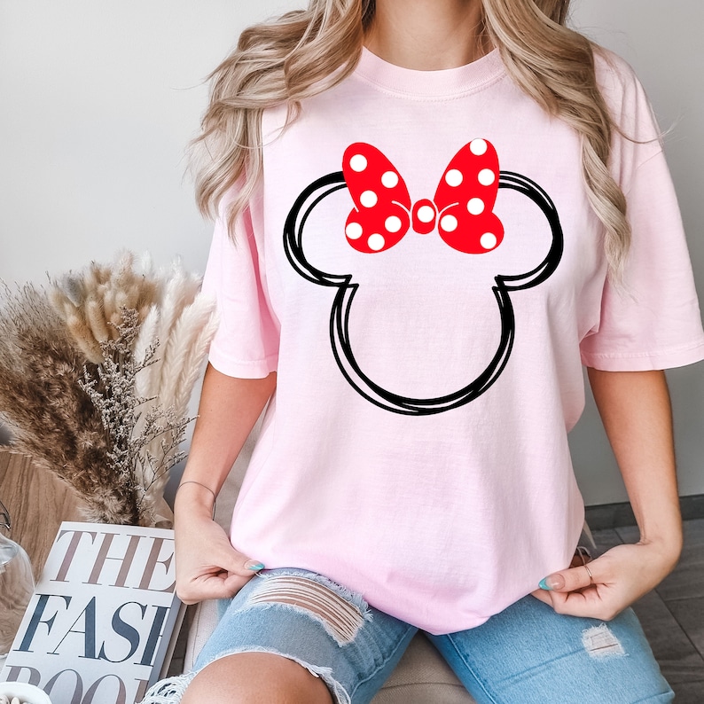 May include: Pink t-shirt with a black outline of Mickey Mouse's head and a red bow with white polka dots.
