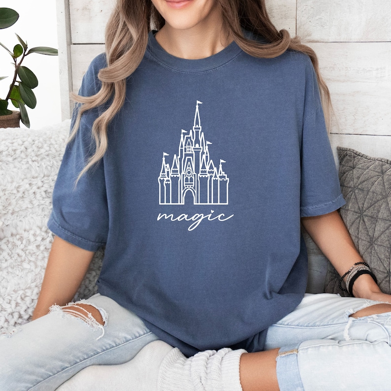 May include: A blue t-shirt with a white outline of Cinderella's castle and the word "magic" underneath.