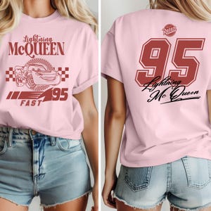 May include: Pink t-shirt with a red graphic of Lightning McQueen, the number 95, and the words "Lightning McQueen" and "Fast". The back of the shirt has a red number 95 with the words "Lightning McQueen" in black.