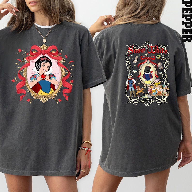 May include: Dark gray t-shirt featuring a Snow White graphic on the front and back. The front design includes a portrait of Snow White holding an apple within a decorative frame. The back design features the text "Snow White" and additional characters.