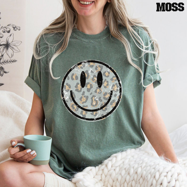 May include: A green t-shirt with a distressed, leopard print smiley face graphic.
