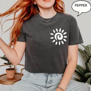 May include: A dark gray cropped t-shirt with a white sun graphic and the word "PEPPER" in a speech bubble.