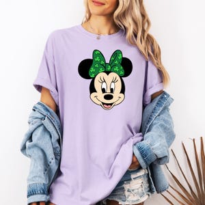 Puede incluir: Camiseta lila claro con un dise&ntilde;o de rat&oacute;n de dibujos animados. El rat&oacute;n tiene orejas negras y un lazo verde adornado con tr&eacute;boles. La camiseta tiene un corte holgado y mangas cortas. Adecuado para el D&iacute;a de San Patricio.