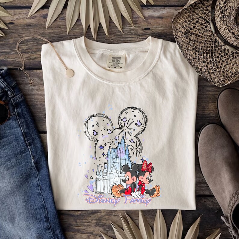 May include: A white t-shirt featuring a sketch of Mickey Mouse ears, Cinderella's castle, and Mickey and Minnie Mouse. The text "Disney Family" is printed below the image.
