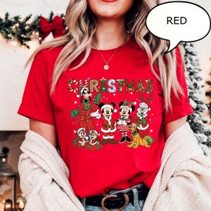 May include: A red t-shirt with a Christmas-themed design featuring cartoon characters. The word "CHRISTMAS" is printed across the front, with a speech bubble that says "RED". The shirt has short sleeves.