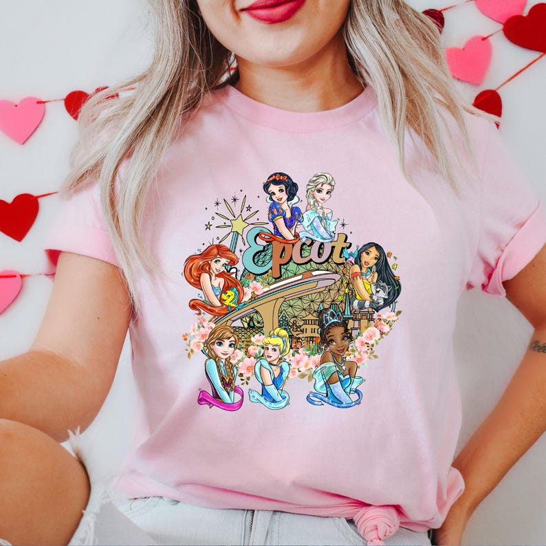 May include: Pink t-shirt featuring a graphic of Disney princesses in front of the Epcot logo and Spaceship Earth. The princesses include Snow White, Ariel, Belle, Cinderella, Pocahontas, Elsa, and Anna.