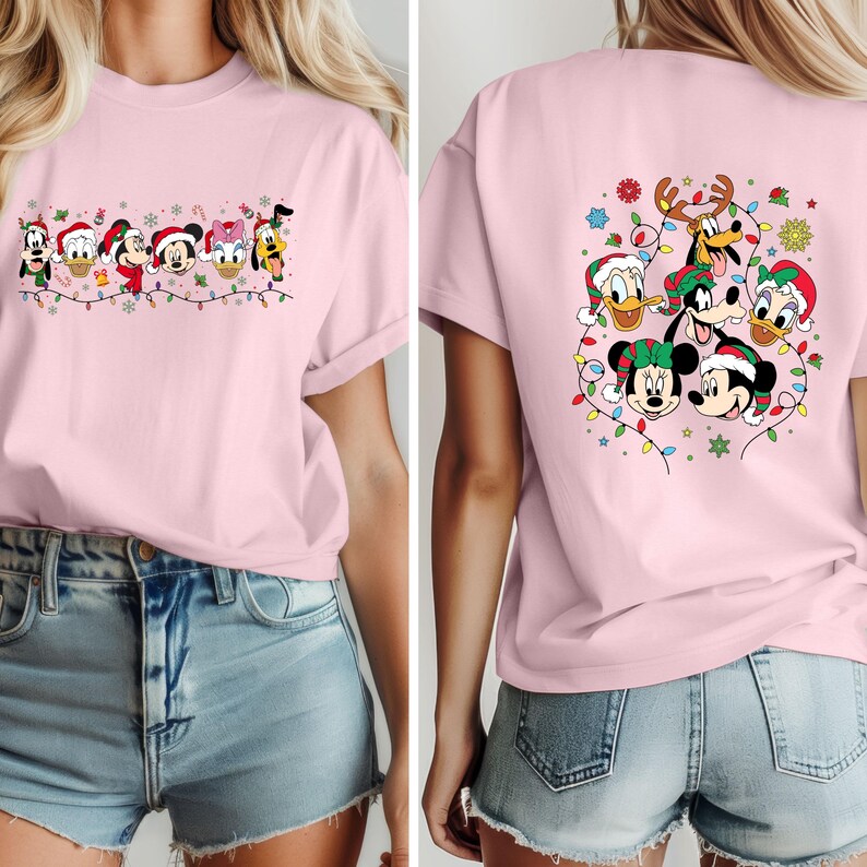 May include: A light pink t-shirt featuring a festive design with Disney characters wearing Santa hats and surrounded by Christmas lights. The front of the shirt displays a line of characters, while the back showcases a group of characters.