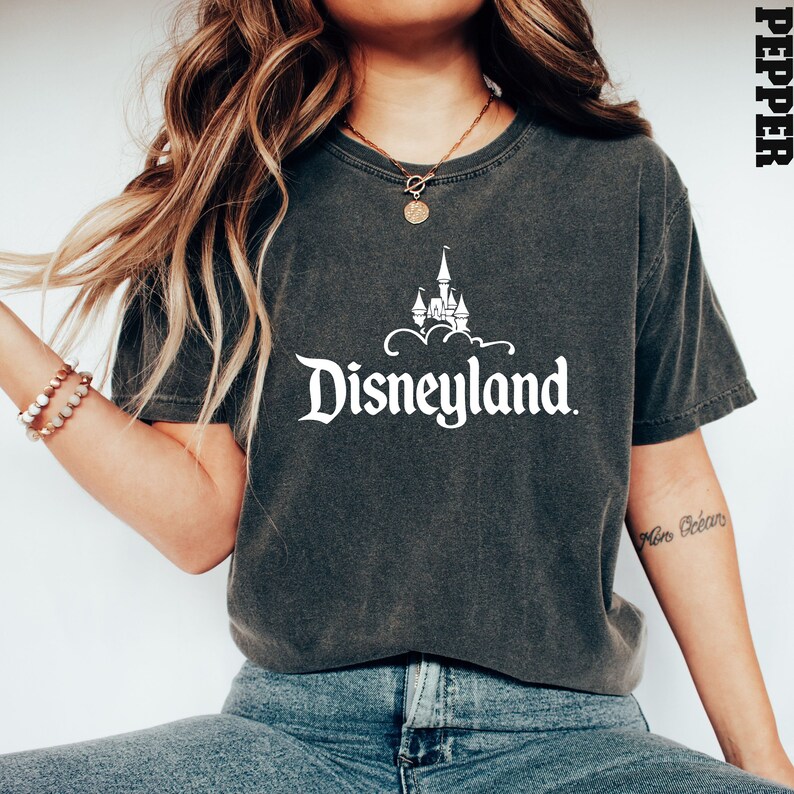 Puede incluir: Camiseta gris oscuro con el logotipo blanco de Disneyland. El dise&ntilde;o incluye el nombre de Disneyland y una ilustraci&oacute;n de un castillo. La camiseta es de estilo casual y c&oacute;modo.