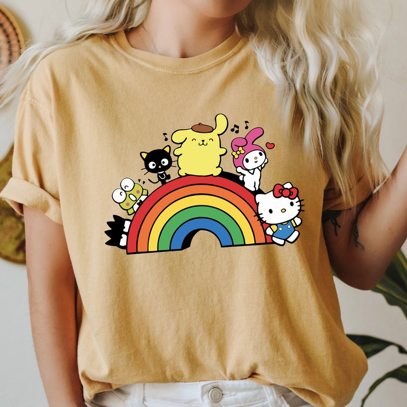 Pode incluir: Uma camiseta amarela com um arco-&iacute;ris e personagens de desenhos animados. Os personagens incluem um gato preto, um cachorro amarelo, um coelho rosa, um sapo verde e um gato vermelho e branco.