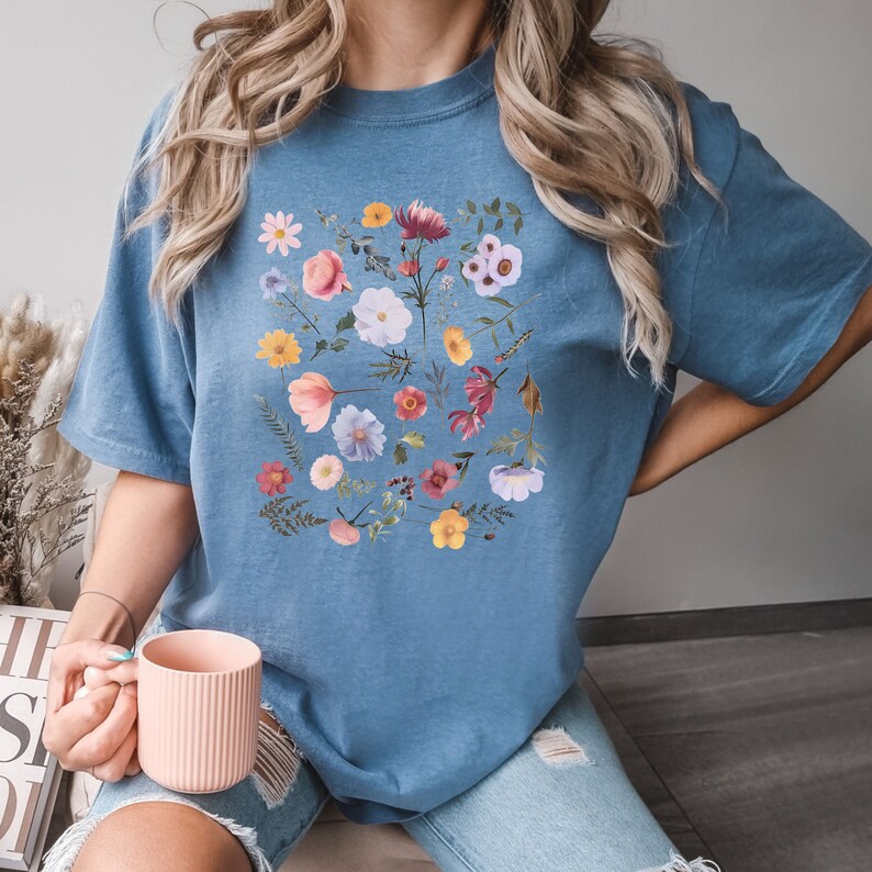 May include: A blue t-shirt with a floral print featuring a variety of flowers in shades of pink, purple, yellow, and red.
