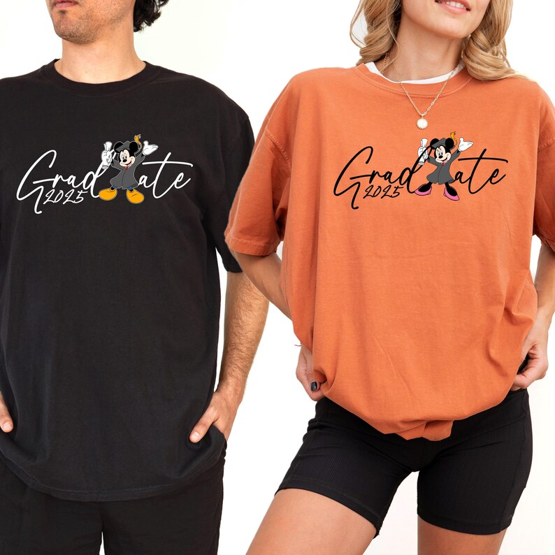 Puede incluir: Dos camisetas con un esquema de color negro y naranja. Las camisetas presentan una imagen de dibujos animados de Mickey Mouse con un gorro y una bata de graduaci&oacute;n. El texto "Graduate 2023" est&aacute; impreso en las camisetas.