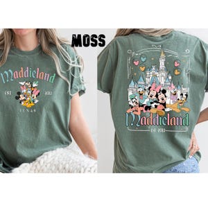 K&ouml;nnte beinhalten: Ein gr&uuml;nes T-Shirt mit einem Aufdruck von Mickey Mouse und seinen Freunden vor einem Schloss. Der Text "Maddieland Est 2023" ist auf dem T-Shirt gedruckt.