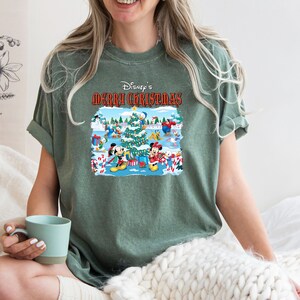 May include: A green t-shirt with a festive Disney Christmas design featuring Mickey Mouse, Minnie Mouse, Donald Duck, and Goofy. The text "Disney's Merry Christmas" is printed on the shirt.