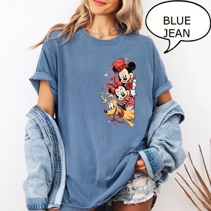 Puede incluir: Camiseta azul vaquero con un gr&aacute;fico de Mickey Mouse, Minnie Mouse y Pluto. Mickey Mouse lleva un sombrero rojo, Minnie Mouse tiene un lazo rojo y Pluto tiene un collar rojo. El texto "BLUE JEAN" est&aacute; en un bocadillo.