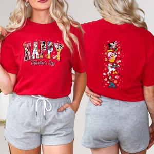 May include: Red t-shirt with the text "HAPPY Valentine's Day" in a colorful design featuring Disney characters. The back of the shirt has a vertical design with Disney characters and hearts. The shirt is paired with gray shorts.