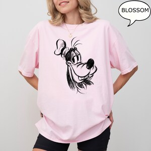 Puede incluir: Una camiseta rosa con un boceto en blanco y negro de la cara de Goofy en la parte delantera. El texto "BLOSSOM" est&aacute; en un bocadillo de di&aacute;logo sobre la imagen.