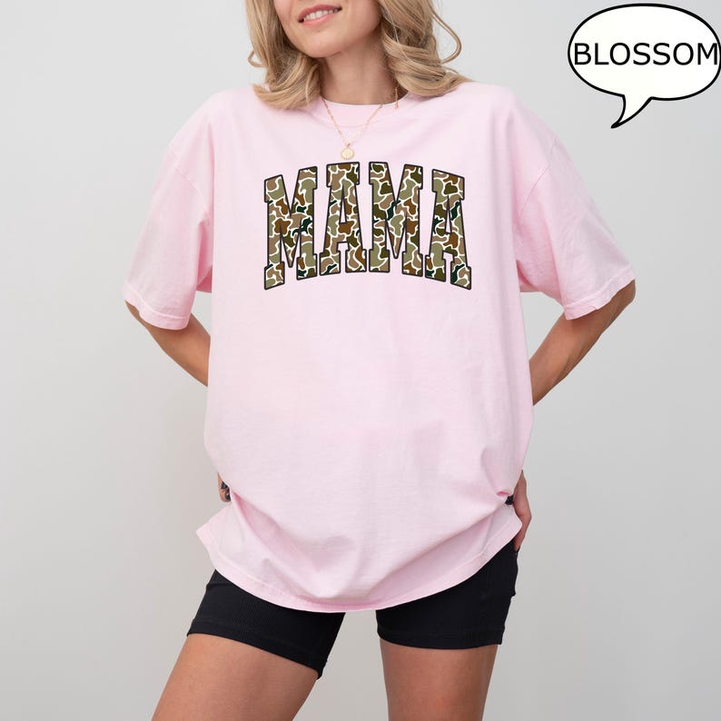 May include: A pink t-shirt with the word "MAMA" printed in a camouflage pattern. The word is in a large, bold font.