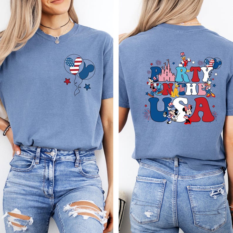K&ouml;nnte beinhalten: Hellblaues T-Shirt mit patriotischem Design. Auf der Vorderseite ist ein Mickey Mouse-f&ouml;rmiger Ballon mit amerikanischem Flaggenmuster zu sehen, und auf der R&uuml;ckseite steht "Party in the USA" mit Mickey Mouse-Figuren und Feuerwerk.