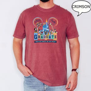 以下が含まれることがあります： ミッキーマウスとその仲間たちが卒業を祝うグラフィックがプリントされた、クリムゾンレッドのTシャツ。シャツのテキストは「2025 Senior Graduate From the Tassel to the Castle」です。