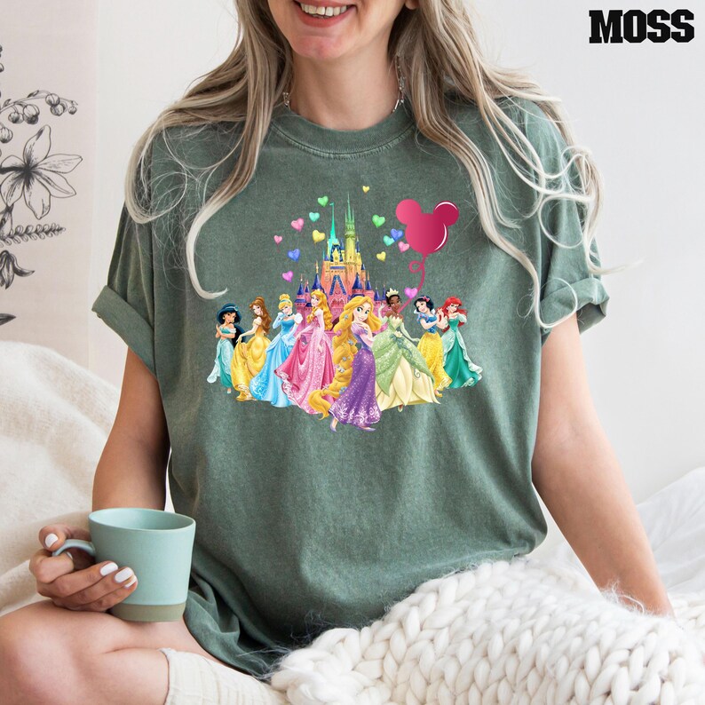 May include: A green t-shirt with a graphic of Disney princesses in front of Cinderella's castle. The princesses are holding hands and there is a pink Mickey Mouse balloon in the air.
