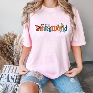 K&ouml;nnte beinhalten: Ein pinkfarbenes T-Shirt mit einem Aufdruck von Disney World-Charakteren und dem Text "Disney World The Original".