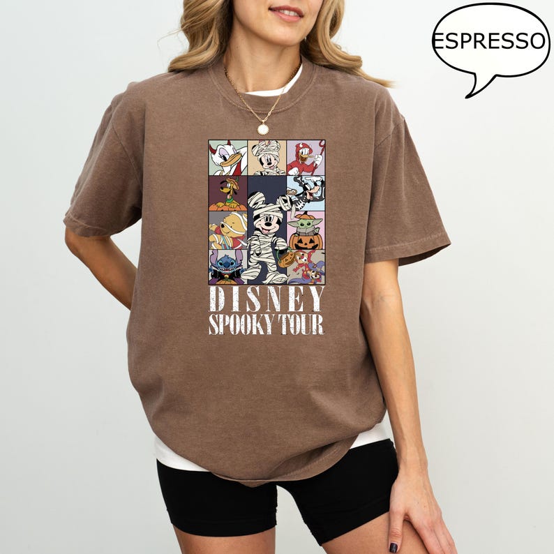 May include: Espresso-colored t-shirt featuring a grid of Disney characters in Halloween costumes. The shirt has the text "DISNEY SPOOKY TOUR" printed below the grid. The shirt is a relaxed fit.