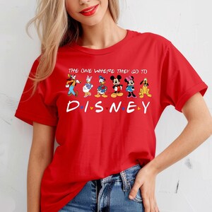 May include: A red t-shirt featuring the text "THE ONE WHERE THEY GO TO DISNEY" above a row of Disney characters. The word "DISNEY" is in large white letters with colorful dots. The characters include Goofy, Daisy Duck, Donald Duck, Mickey Mouse, Minnie Mouse, and Pluto.