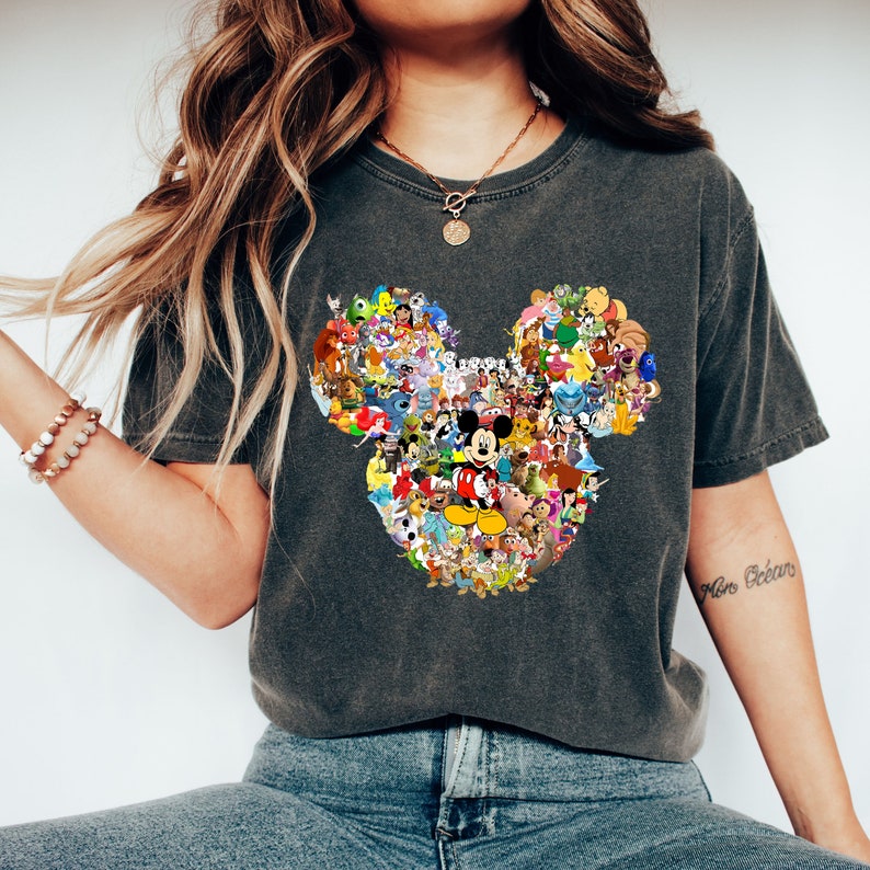 May include: A dark gray t-shirt with a large Mickey Mouse head design made up of various Disney characters. The design is in a collage style with many different colors and characters.