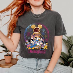 May include: A black cropped t-shirt with a graphic of Mickey Mouse and friends celebrating Disneyland's 70th anniversary. The graphic features a castle, fireworks, and the text "70th Anniversary" and "Disneyland Resort".