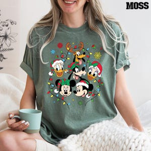 May include: A green t-shirt with a Christmas-themed design featuring Mickey Mouse, Minnie Mouse, Donald Duck, Goofy, and Pluto. The characters are surrounded by colorful Christmas lights.