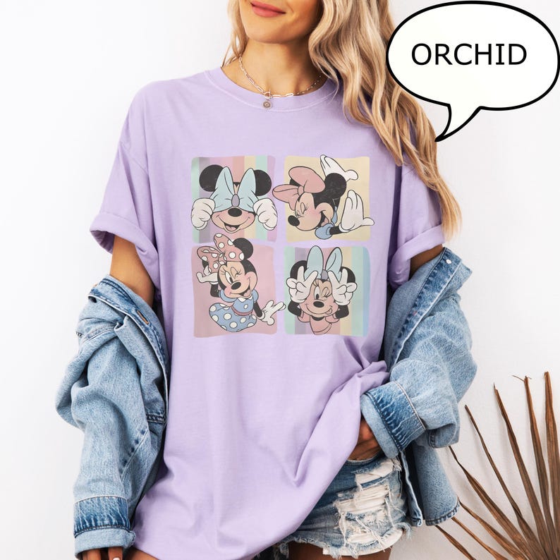 Puede incluir: Camiseta color orqu&iacute;dea con un gr&aacute;fico de cuatro paneles de Minnie Mouse en varias poses. El gr&aacute;fico tiene bloques de color pastel. La palabra "ORCHID" est&aacute; en un bocadillo. La camiseta tiene un corte holgado.