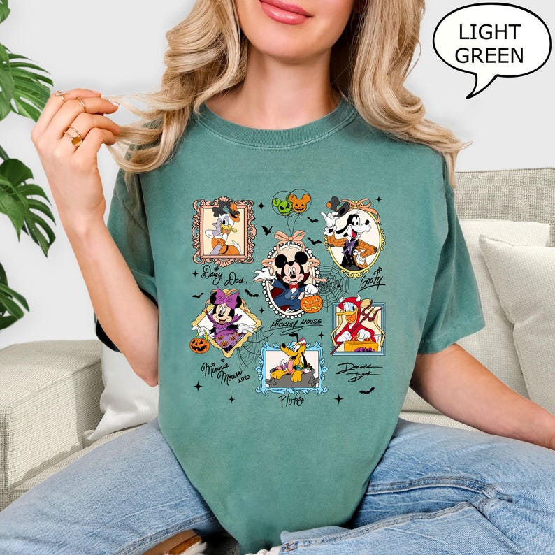 Puede incluir: Una camiseta verde claro con ilustraciones enmarcadas de personajes de Disney con disfraces de Halloween. Los personajes incluyen Mickey Mouse, Minnie Mouse, Donald Duck, Goofy y Pluto. La camiseta tiene el texto "Mickey Mouse" y "Minnie Mouse".