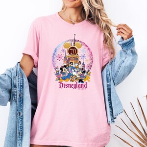 May include: Pink t-shirt with a graphic of Mickey Mouse and friends celebrating Disneyland's 70th anniversary. The graphic features the Disneyland castle, fireworks, and the text "Disneyland Resort".